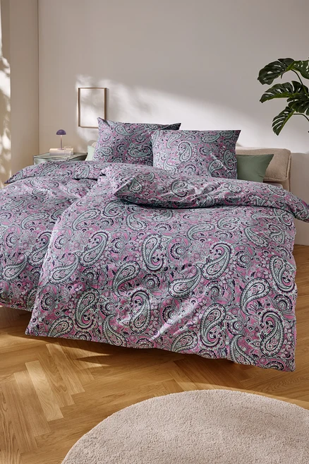 Detailný záber na posteľ s ružovou posteľnou bielizňou s paisley vzorom.