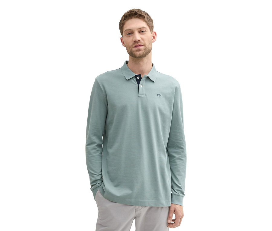 Muž v mätovo sivom piké polokošeli s dlhým rukávom Tom Tailor a v sivých nohaviciach stojí na bielom pozadí.