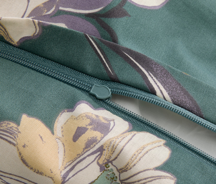 Detailný záber na zips na zelenkastej látke s kvetinovým vzorom.