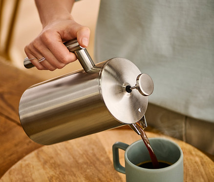 Žena nalieva kávu z dvojstennej kanvice french press z ušľachtilej ocele s objemom 900 ml do hrnčeka.