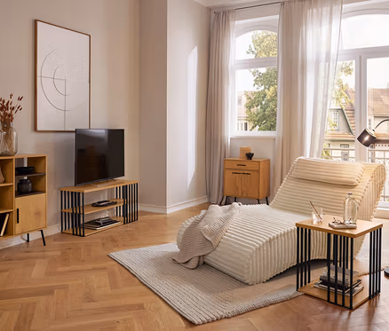Moderná obývačka s krémovou leňoškou na svetlom koberci, drevenou skrinkou, TV stolíkom a príručným stolíkom. Veľké okná so závesmi s výhľadom von.