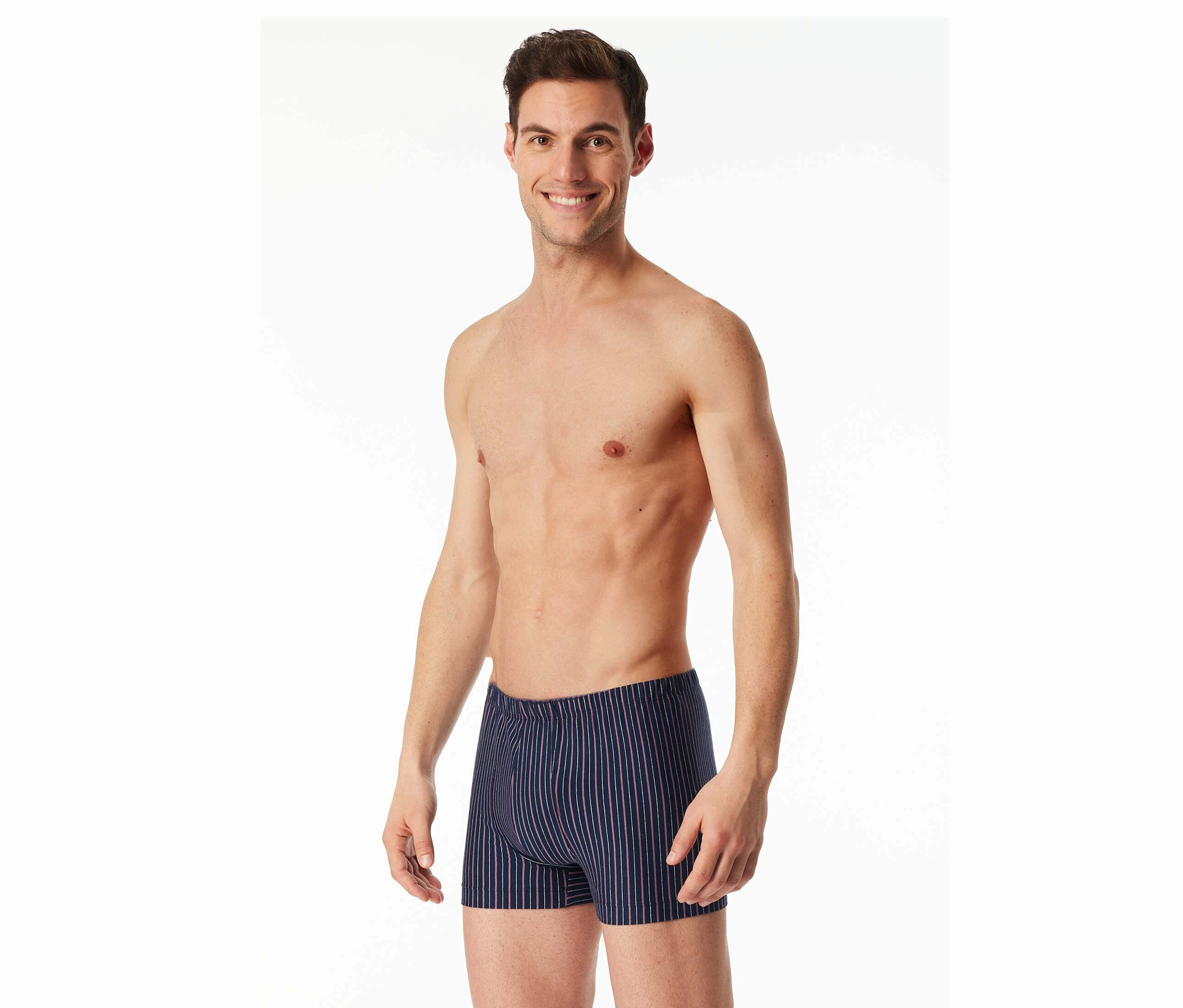 Usmievajúci sa muž s odhalenou hornou časťou tela má na sebe pruhované boxerky na bielom pozadí.