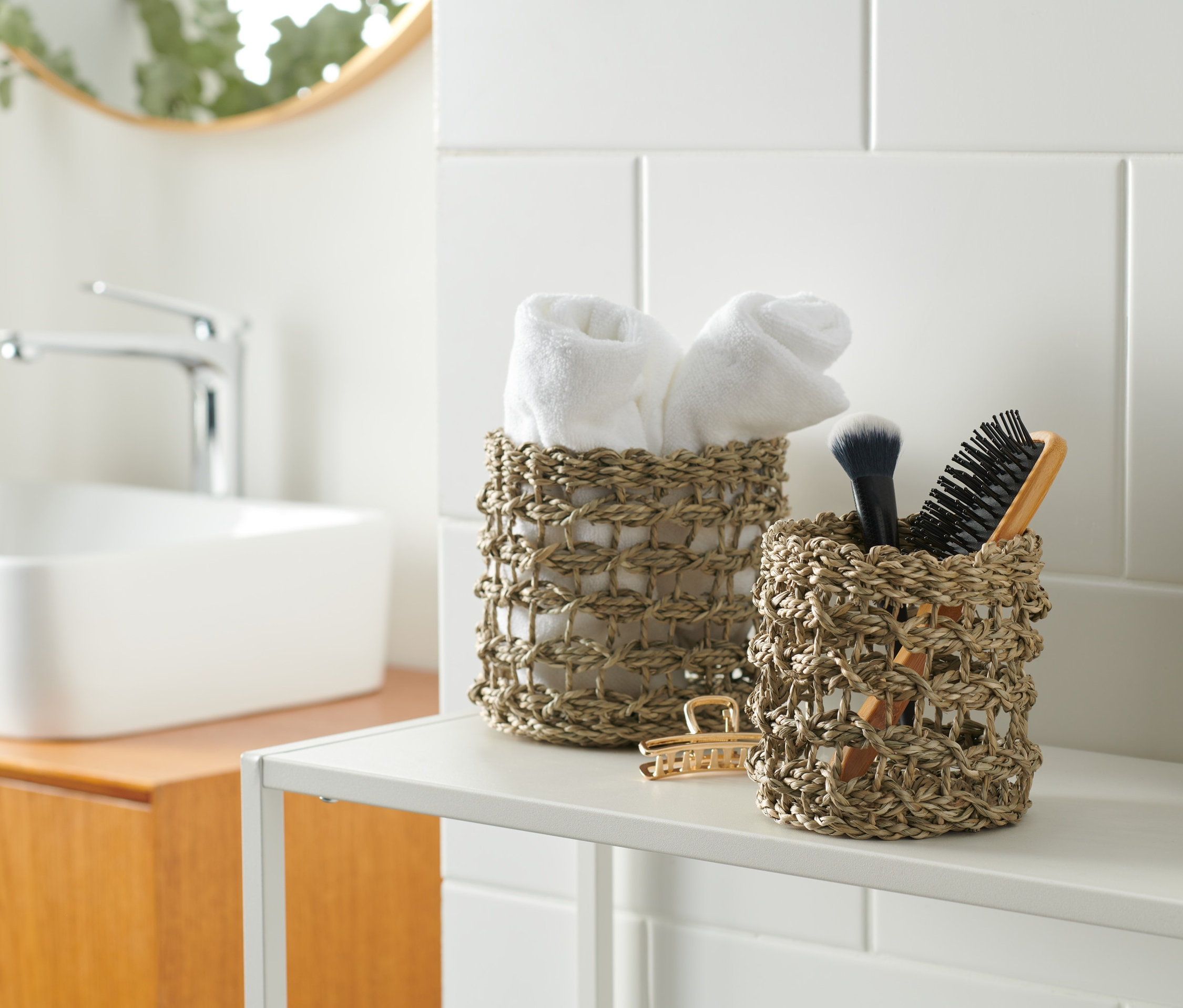 Dva úložné košíky na poličke v kúpeľni. V jednom košíku sú uteráky, v druhom kozmetické štetce.