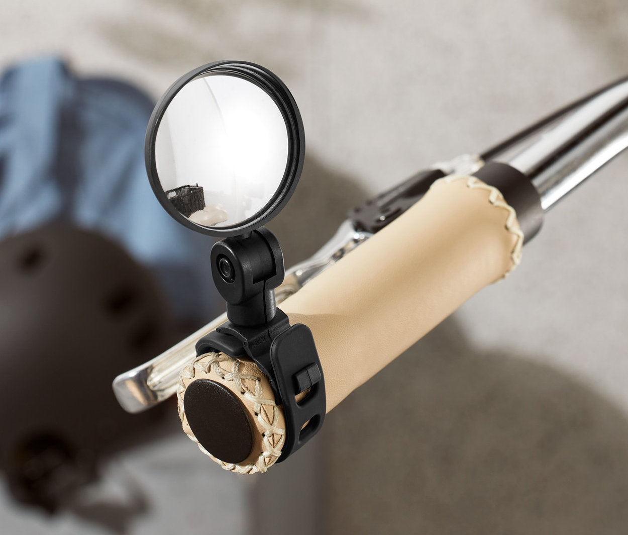 Detail bicykla so zrkadlom na riadidlách. V pozadí je prilba a bunda.