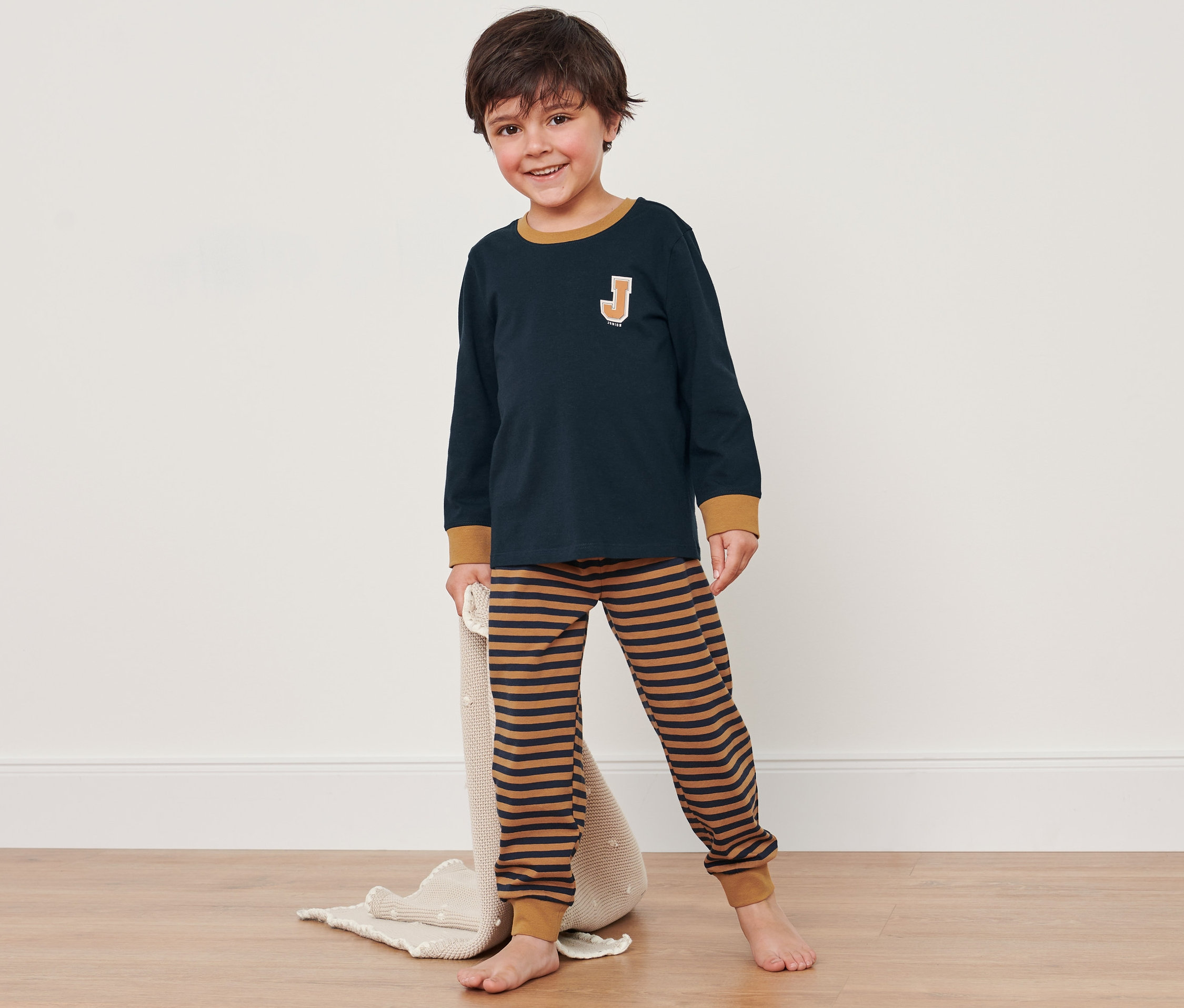 Chlapec v modro-hnedém pyžame stojí na podlahe a drží deku.