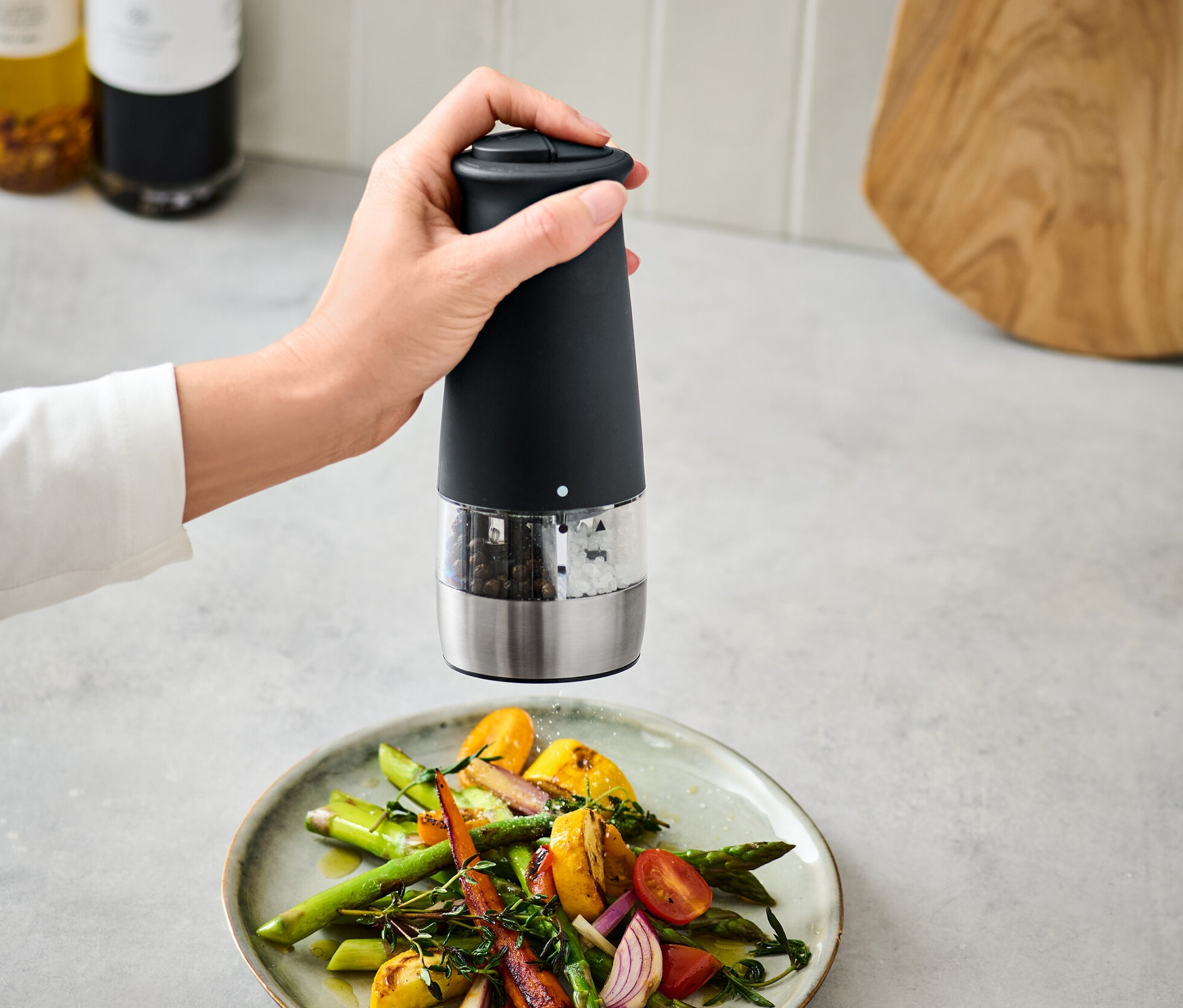 Ruka používa elektrický mlynček na soľ a korenie 2 v 1 nad tanierom zeleniny.