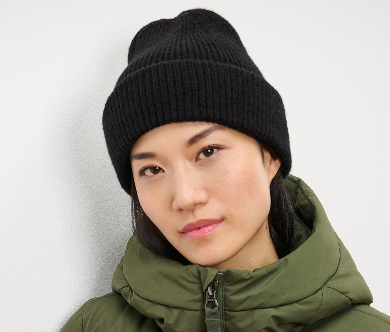 Žena má na sebe čiernu pletenú čiapku a zelenú bundu.