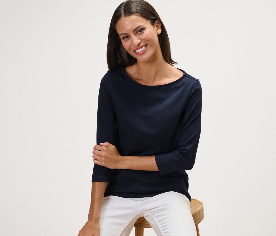 Žena sedí na stoličke a má na sebe námornícke modré tričko s trojštvrťovými rukávmi.