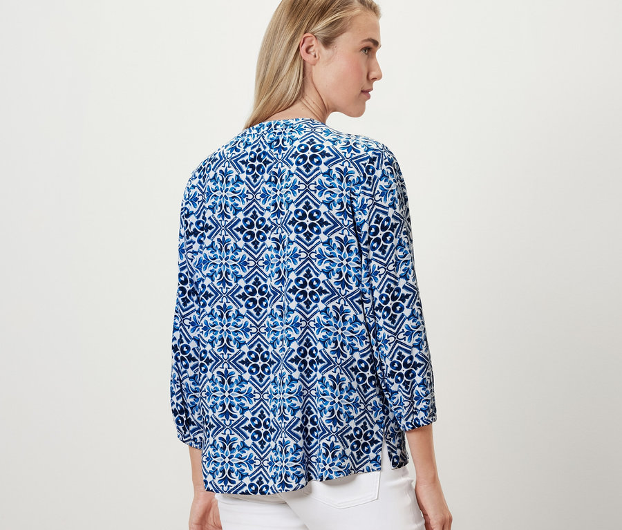Žena má na sebe modrú tunikovú blúzku s potlačou.