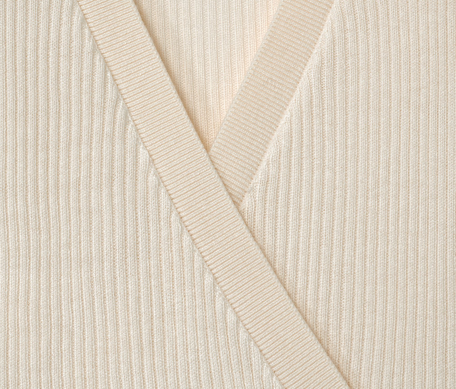 Detailný záber na detský pletený svetrík krémovej farby.