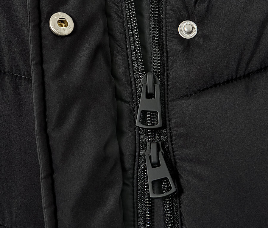 Detail čierneho prešívaného kabáta s kapucňou, zobrazujúci zips a patentky.