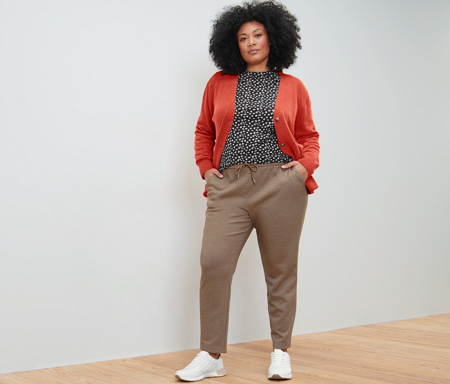 Žena pózuje v béžových teplákových nohaviciach, tričku s dlhými rukávmi a celoplošnou potlačou a kardigáne s výstrihom do V.