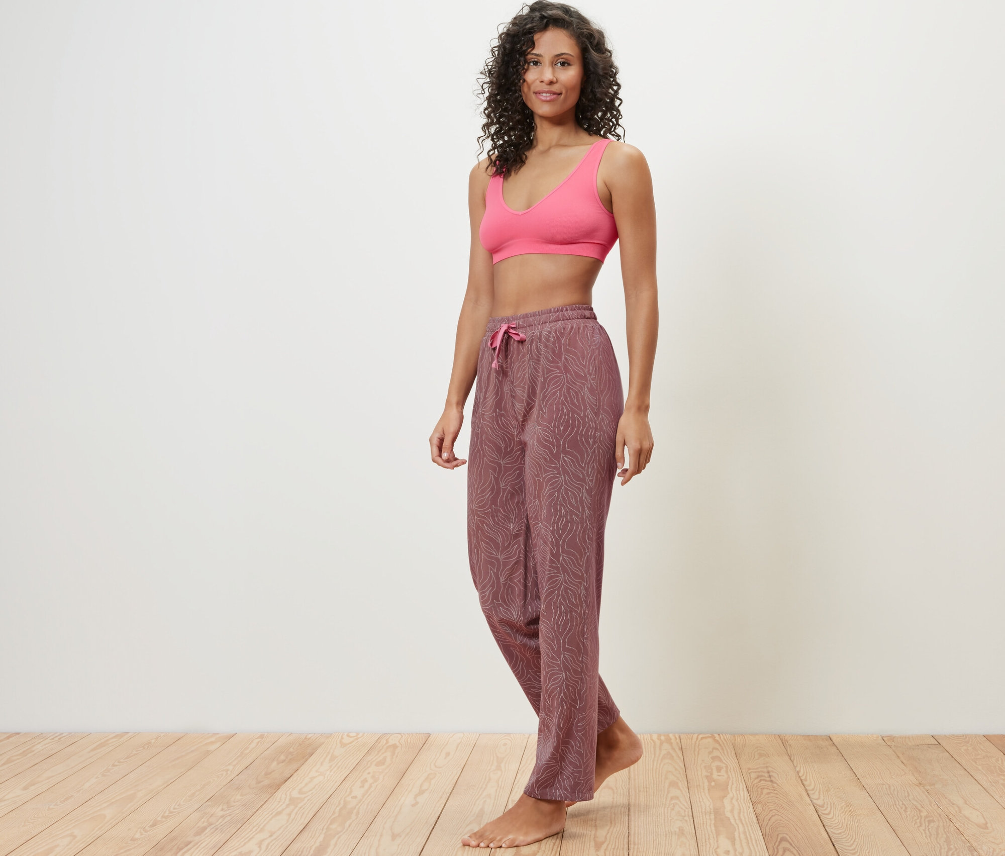 Žena pózuje v ružovej športovej podprsenke a pyžamových nohaviciach.