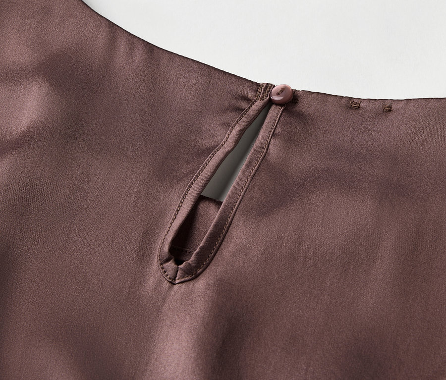 Detail hnedej saténovej blúzky s kľúčovou dierkou a zapínaním na gombík na zadnej strane krku.