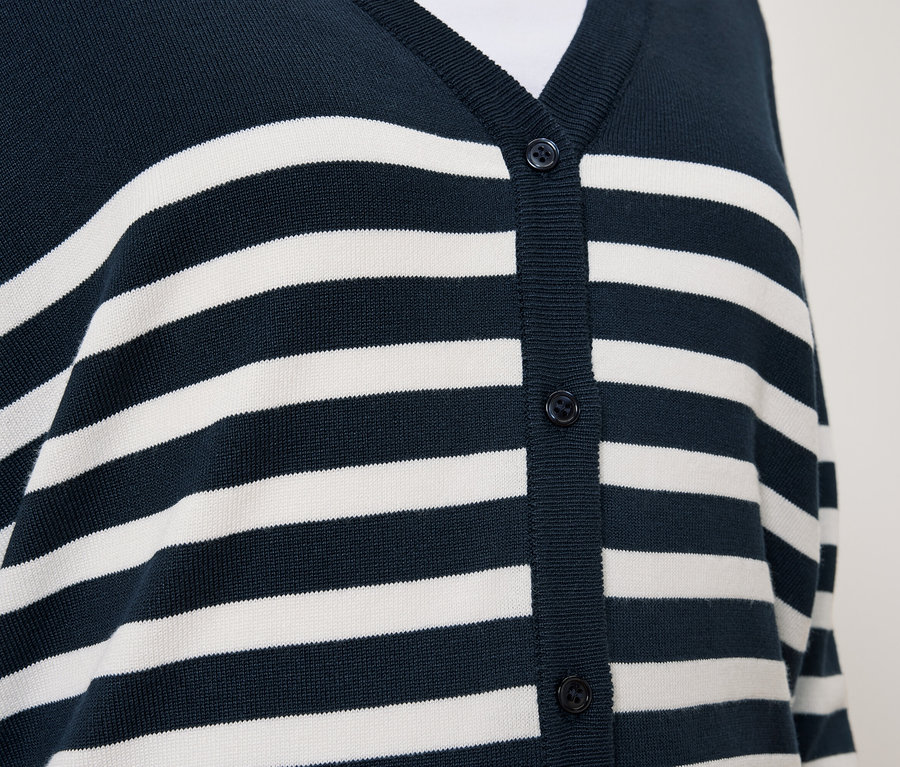 Detail modrého svetra s bielymi pruhmi a gombíkmi.