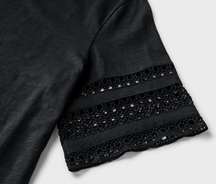 Detail čierneho trička s výšivkou na rukáve.