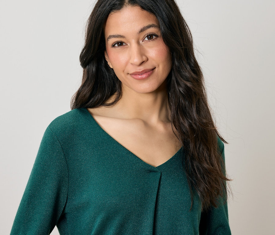 Portrét ženy s dlhými vlnitými hnedými vlasmi v zelenom svetri s výstrihom do V.