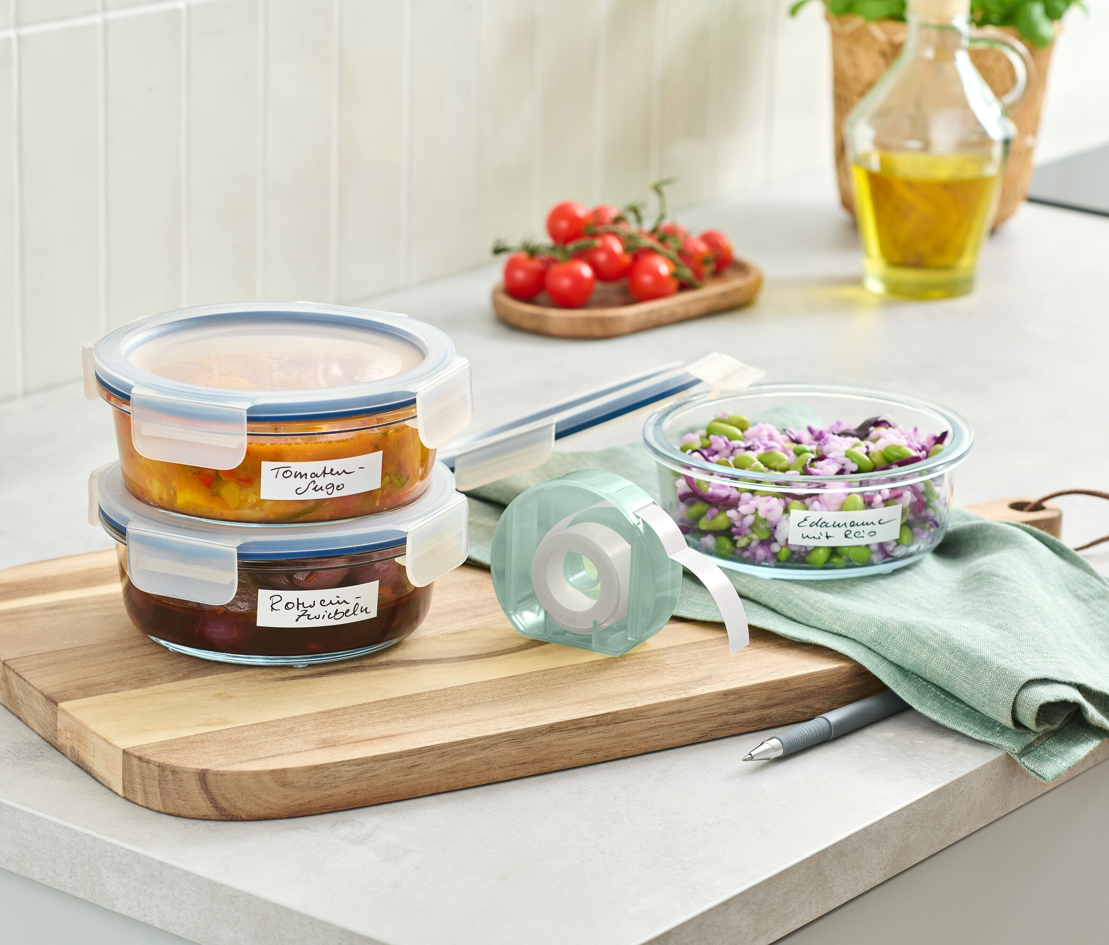 Dve sklenené nádoby s jedlom poukladané na drevenej doske vedľa rolky s etiketami.