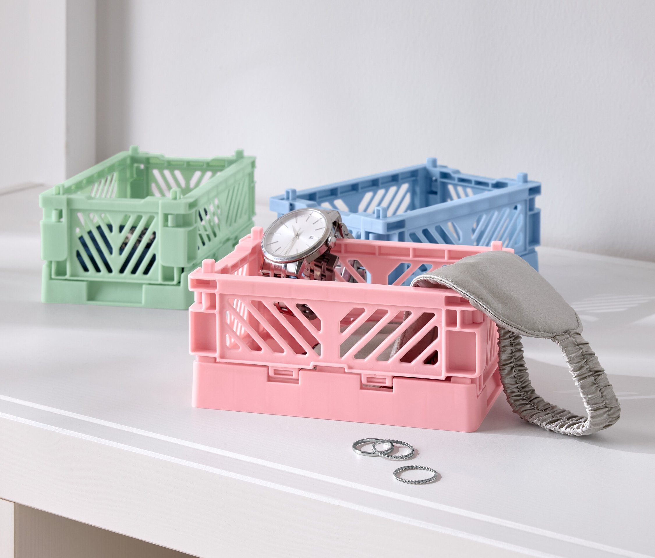 Tri farebné skladacie škatule na stole, jedna ružová s hodinkami, jedna modrá a jedna zelená.
