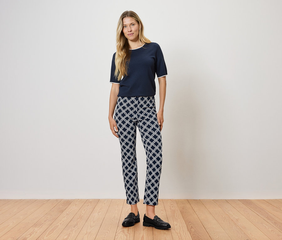 Žena stojí na drevenej podlahe a má na sebe tmavomodré tričko a vzorované nohavice.