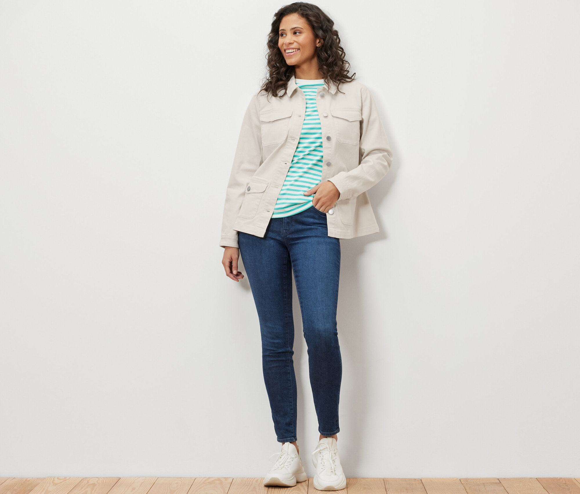 Žena má na sebe džínsovú bundu s cargo vreckami, modré džínsy a biele tenisky.