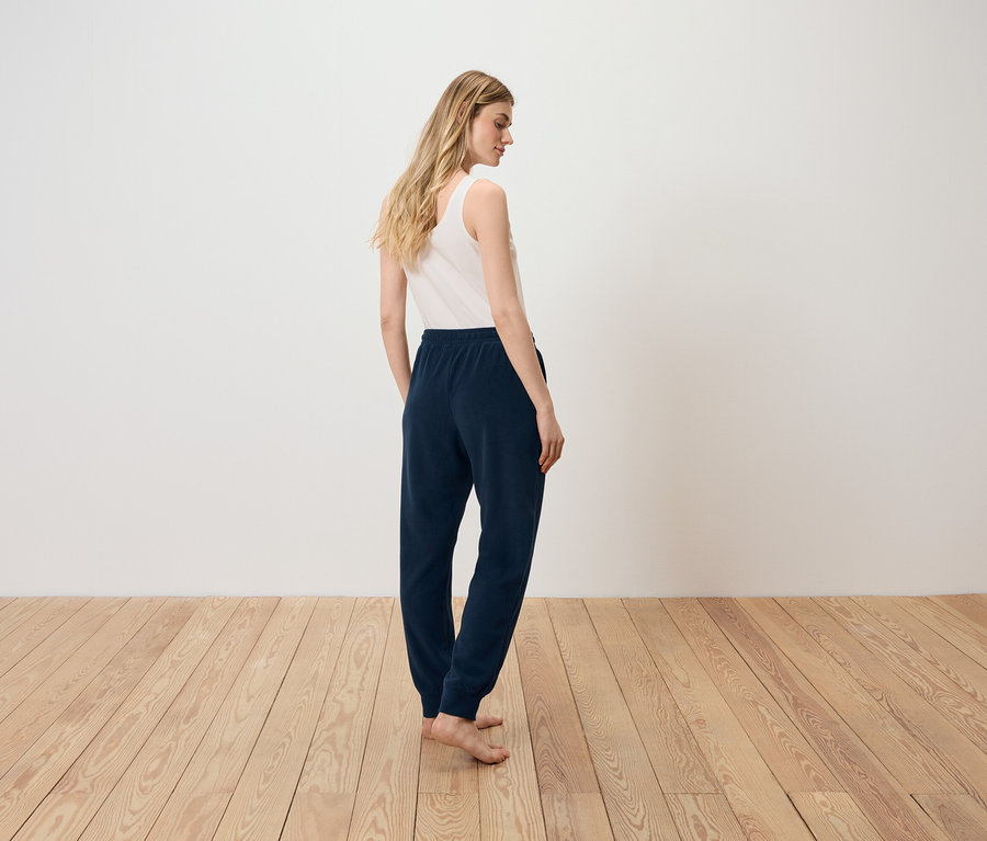 Žena stojí chrbtom k fotoaparátu, má na sebe biele tielko a tmavomodré tepláky.