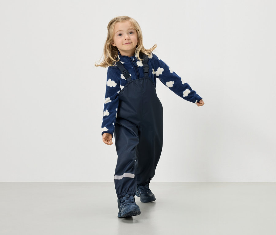 Blondínka má na sebe tmavomodrú fleecovú bundu s obláčikovým vzorom a tmavomodré nohavice s podväzkami.
