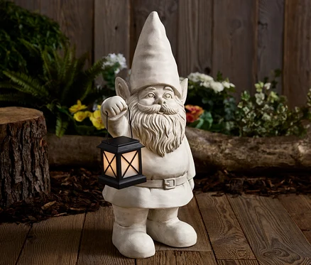 Kamenný záhradný trpaslík drží čiernu lampu pred dreveným pozadím.