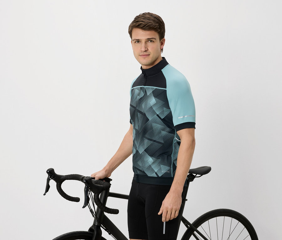 Muž v cyklistickom drese s modrozelenými rukávmi drží čierny bicykel.