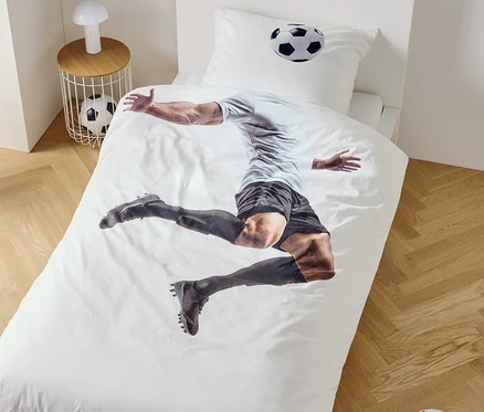 Na obliečke na posteľ je zobrazený futbalista v skoku, vedľa nočný stolík s lampou a futbalovou loptou.