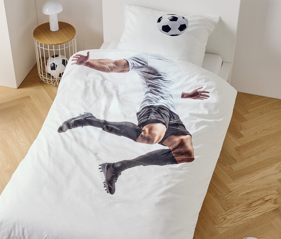Na obliečke na posteľ je zobrazený futbalista v skoku, vedľa nočný stolík s lampou a futbalovou loptou.