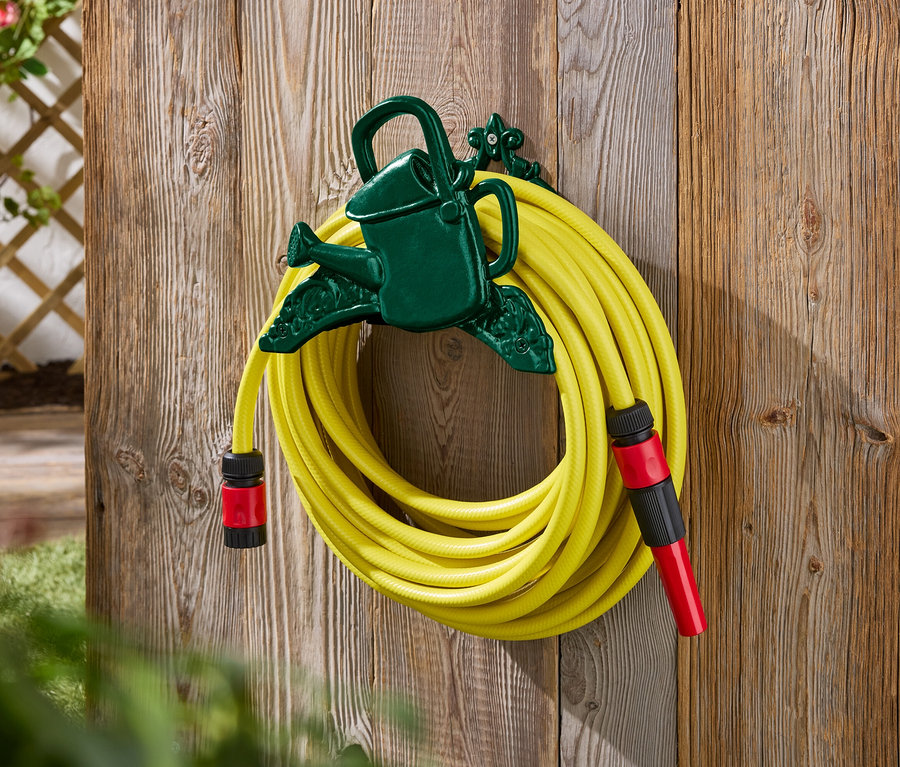 Žltá záhradná hadica pripevnená k zelenému držiaku v tvare kanvy na drevenej stene.