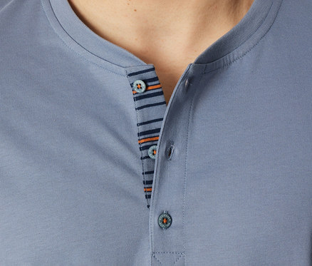 Detailný záber osoby v modrosivom tope z krátkeho pyžama SCHIESSER, zobrazujúci Henley výstrih s tromi gombíkmi a pruhovanú légu v tmavomodrej a oranžovej farbe.