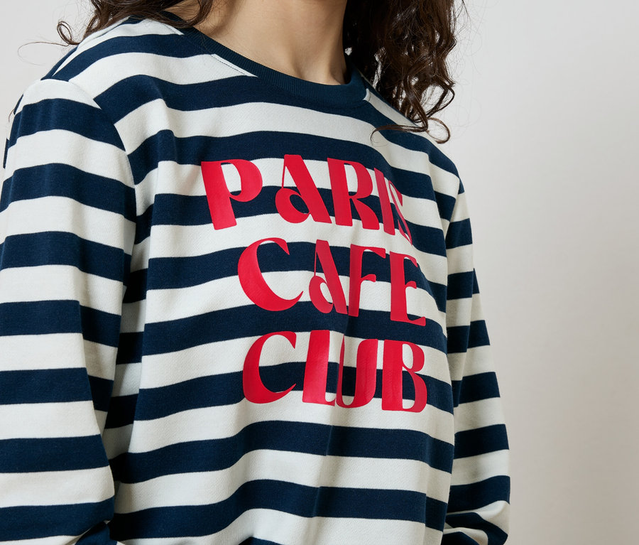Žena má na sebe modro-biele pruhované tričko s nápisom "Paris Cafe Club" červenou farbou.