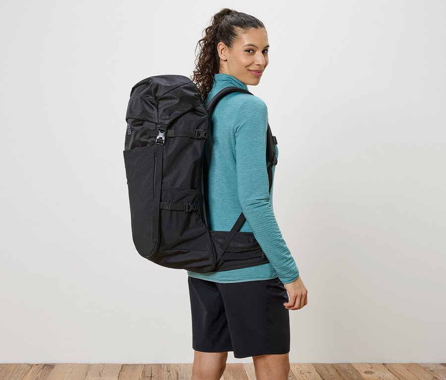 Žena s čiernym batohom prehodeným cez ramená sa pozerá cez plece.