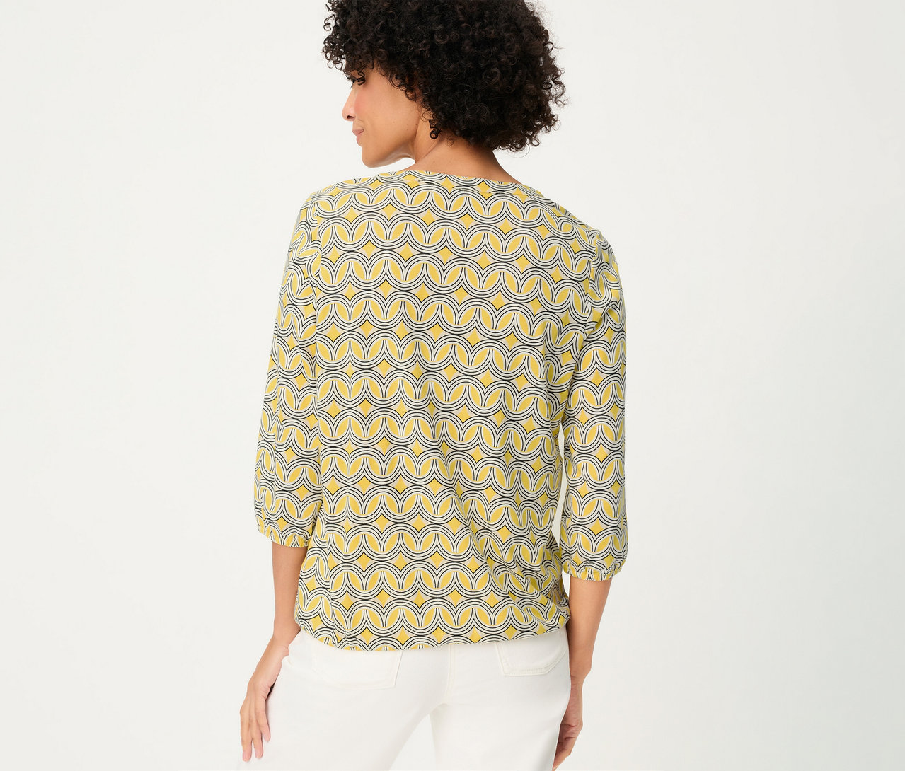 Žena zozadu v 3/4 blúzkovej košeli Olsen so žltým vzorom a bielych nohaviciach.