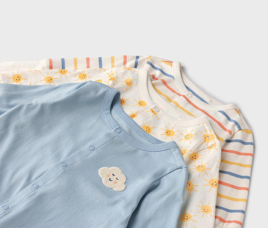 Detail troch detských overalov: svetlomodrý s obláčikovou aplikáciou, biely so slnkami a pruhovaný.
