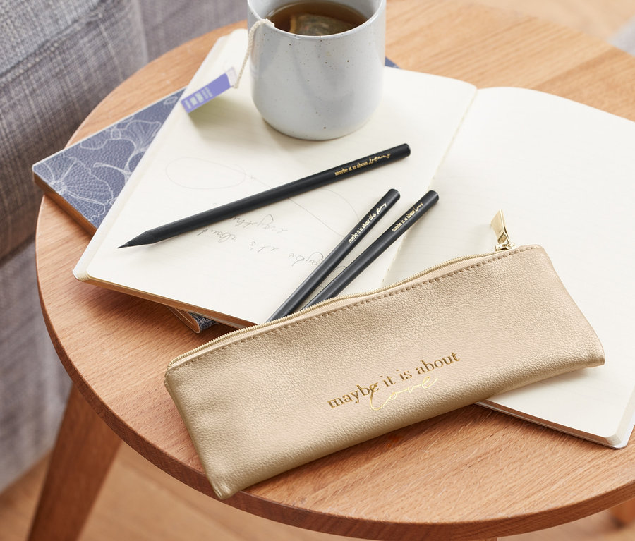 Na stole leží peračník s 3 ceruzkami, zápisník a šálka čaju.