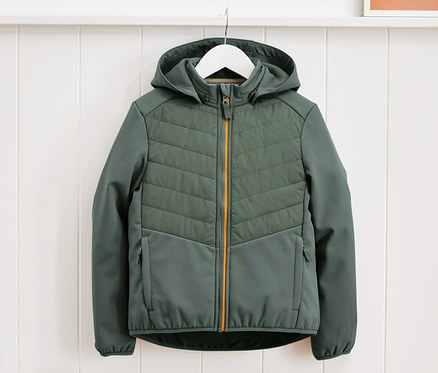 Zelená hybridná bunda visí na bielom vešiaku pred bielym stenovým panelom.