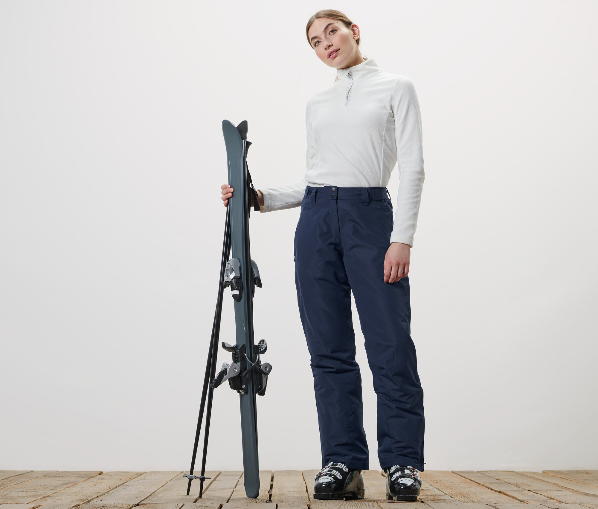 Žena drží lyže a má na sebe lyžiarske nohavice.