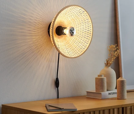 Nástenná lampa s bambusovým tienidlom visí na stene nad drevenou komodou.