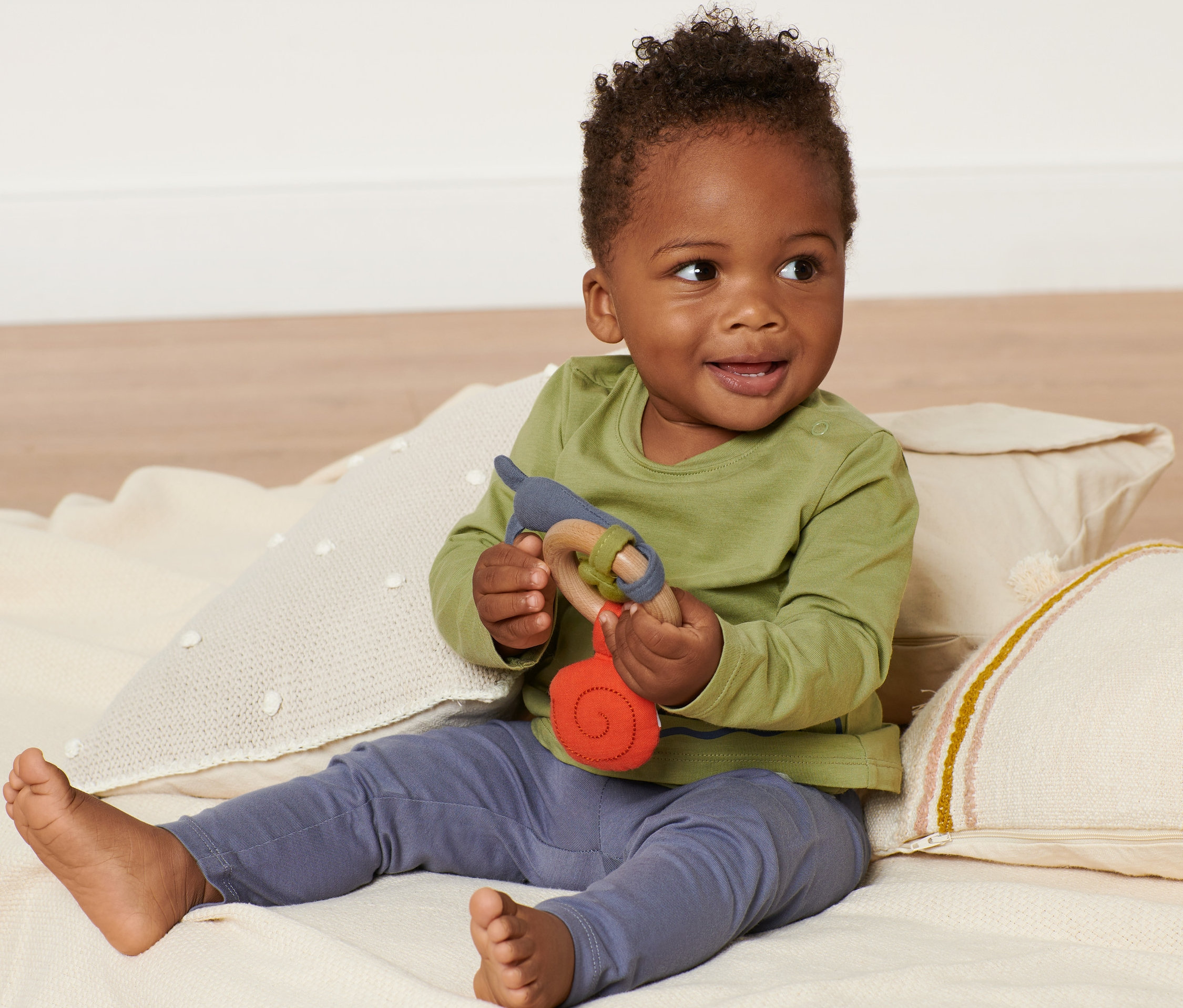 Usmievajúce sa dieťa sedí na deke a drží hmatovú hračku.