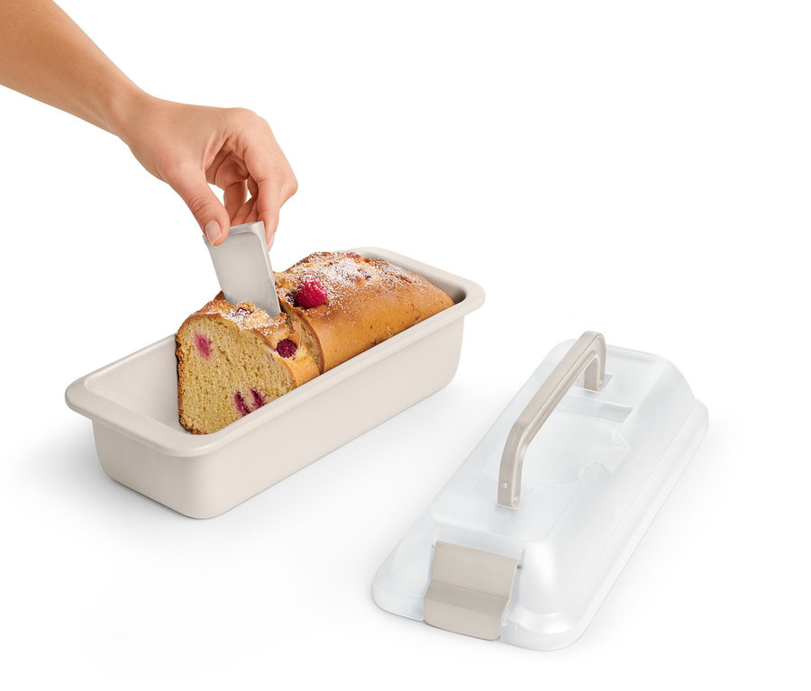 Ruka krája kúsok malinového koláča v hranatej forme na pečenie s vekom.