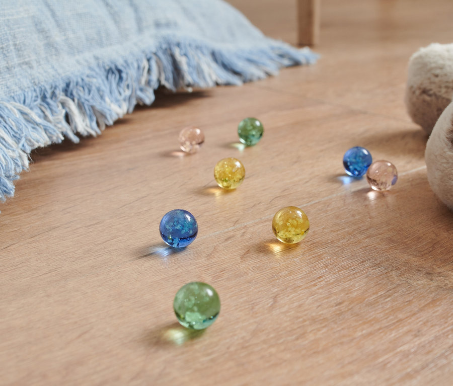 Svetelné guľôčky rôznych farieb ležia na podlahe vedľa plyšového psa a modrej deky.