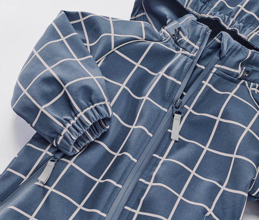 Detail detského softshellového overalu s kockovaným vzorom a zipsom.