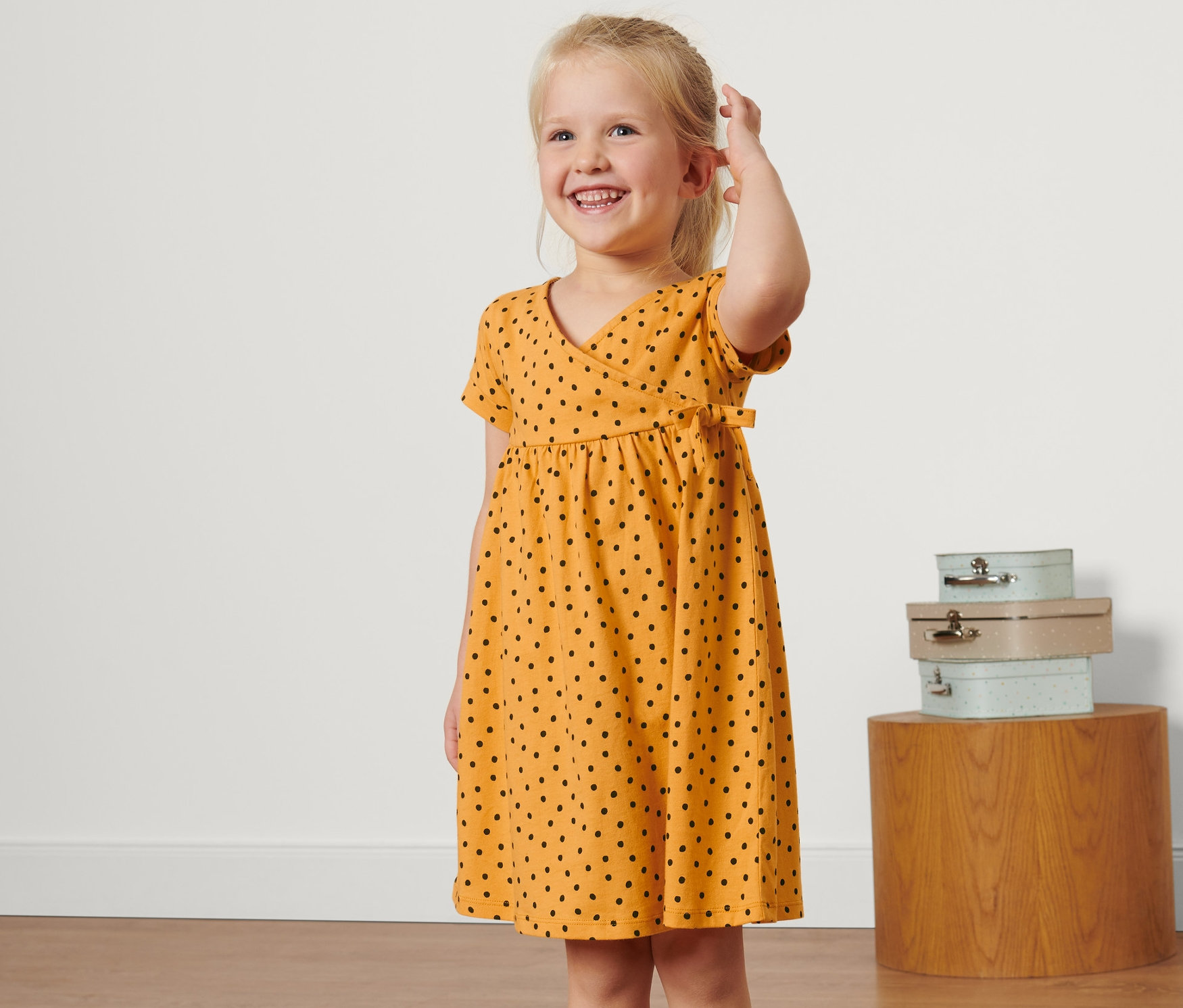 Usmievavé sa blond dievča má na sebe žlté detské džersejové šaty s čiernymi bodkami.