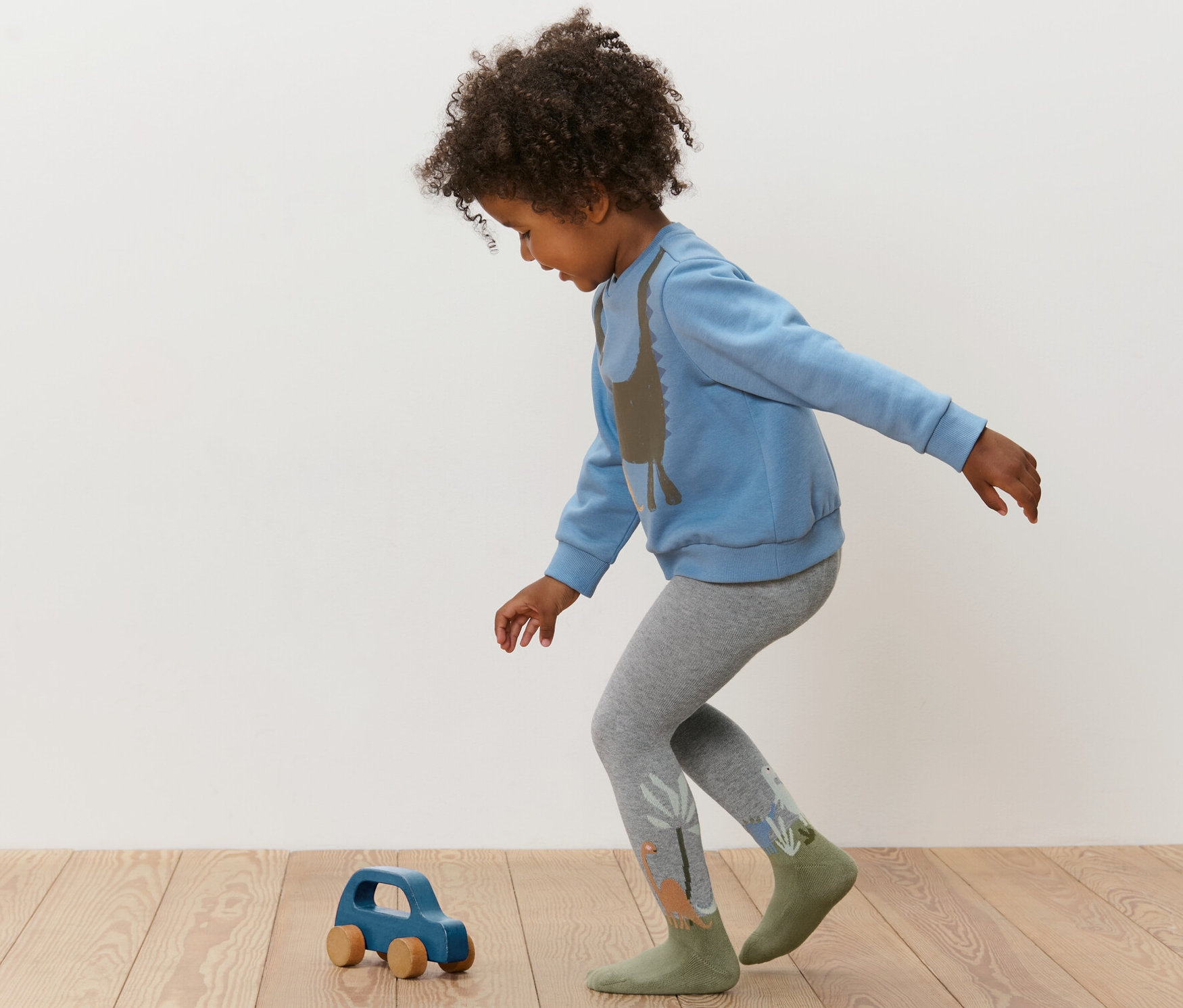 Dieťa sa hrá s modrým dreveným autíčkom a má na sebe modrú mikinu a sivé pančuchové nohavice. Detské pančuchové nohavice, 3 páry, modré.