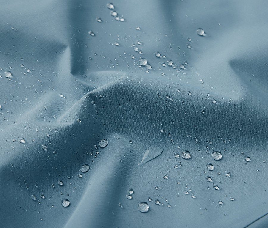 Detailný záber na modrú funkčnú outdoorovú bundu s kvapkami vody.