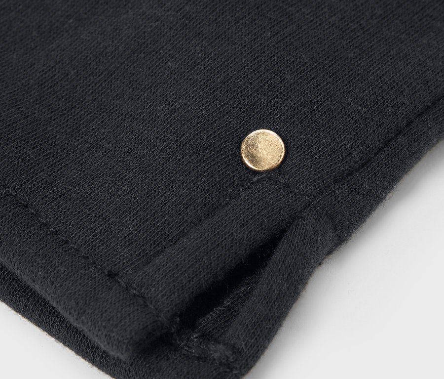 Detailný záber na čiernu látku s malým zlatým gombíkom.