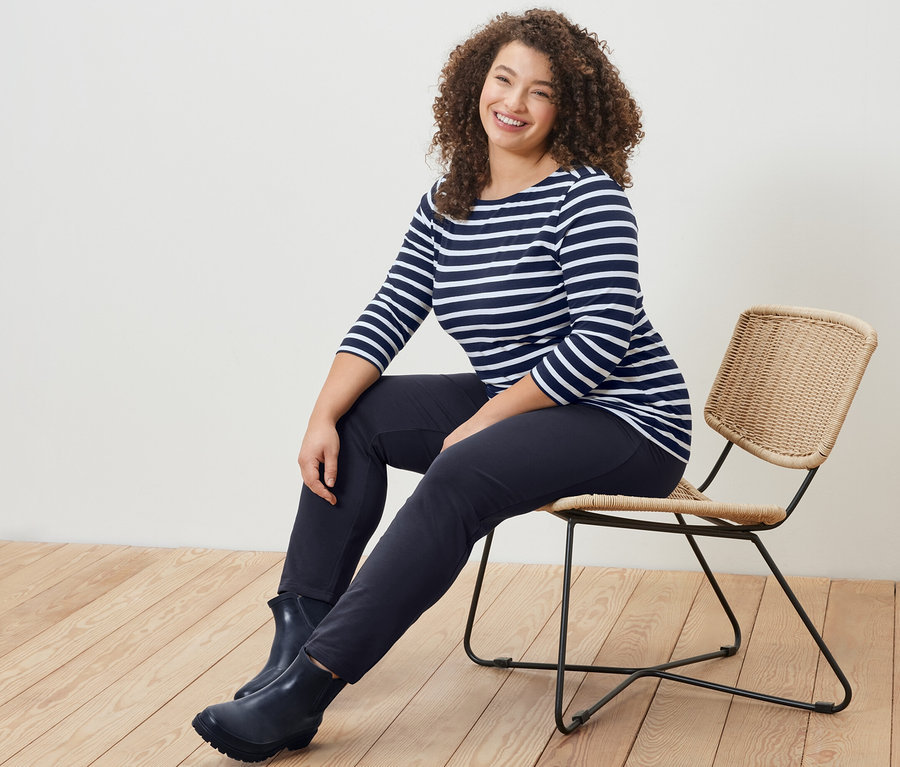 Žena sedí na stoličke v prúžkovanom tričku s trojštvrťovými rukávmi a námorníckych modrých pohodlných nohaviciach.